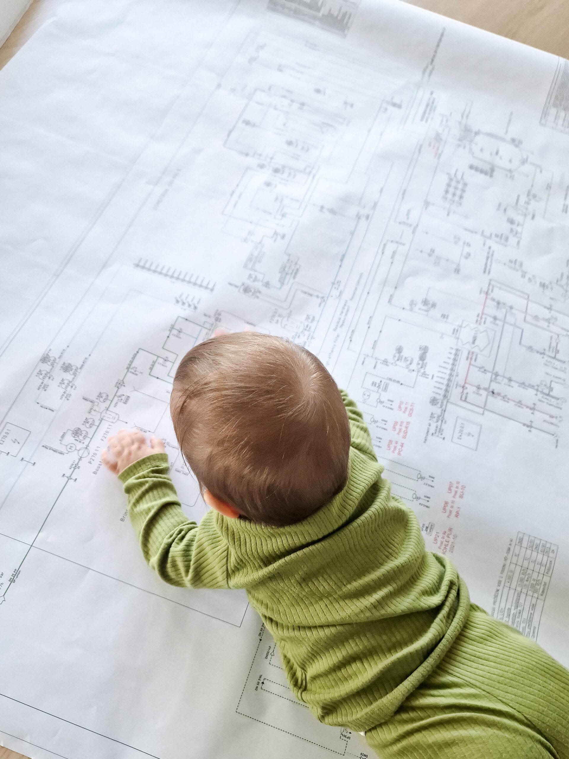 Beba u zelenoj odeći leži na tehničkom crtežu i posmatra šemu instalacija