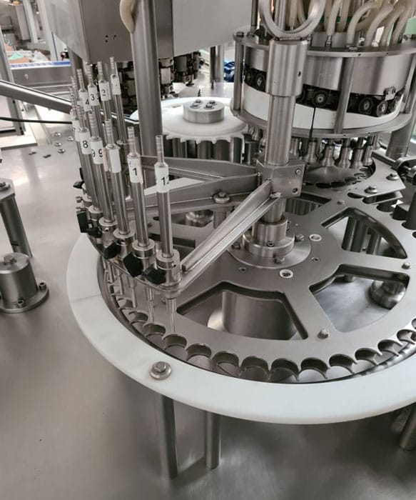 Detalj rotacione COMAS mašine za punjenje bočica sa numerisanim diznama i mehaničkim mehanizmom za precizno doziranje